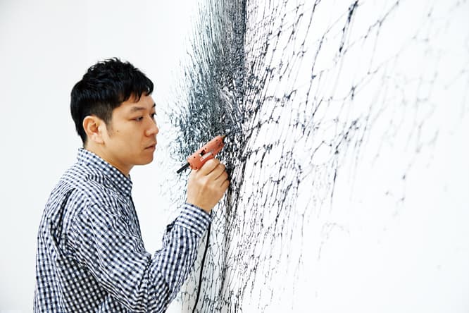 オフィスだった部屋の白い壁に直接、グルーガンで描いていく名和晃平。“塗り重ねて”いくうちに少しずつ盛り上がっていく、ドローイングと彫刻の中間のような作品。このほかに物体の物理的な運動を利用して描いたドローイングを出品している。
