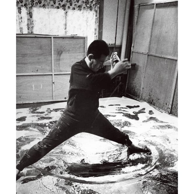 具体を代表する天才的な抽象画家、白髪一雄は1924年尼崎生まれ。天井から吊るしたロープを持ちながら足を使って描く作品で知られる。これは63年のアトリエでの制作風景。写真提供／尼崎市総合文化センター。