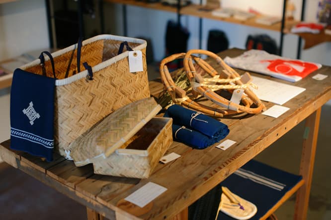 千葉の房総の農家で作られたかご（写真前）や山形の田麦俣で作られたくろもじの木を時間をかけて曲げて作ったかんじき、坂本が作った版画をモチーフにしたＴシャツなどが並ぶ。