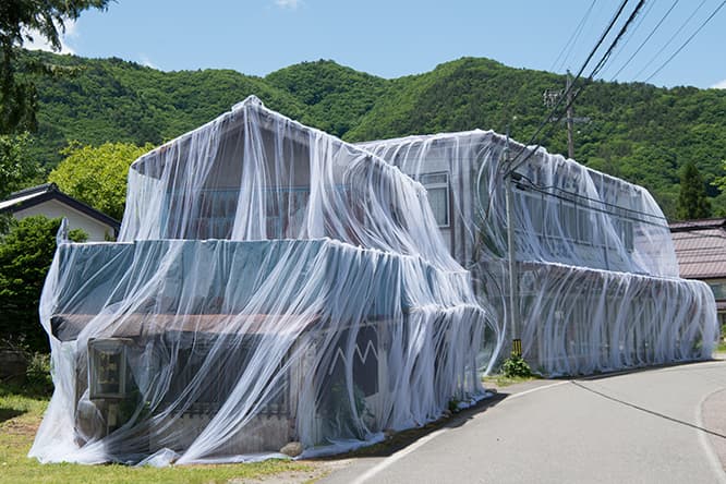 ケイトリン・RC・ブラウン＆ウェイン・ギャレット《ベールの向こうに》。空き家や空き店舗に透き通った白いベールをかぶせた。風に揺れるベールの向こうに、今では草や花の住処になった建物が見える。　photo_Tsuyoshi Hongo
