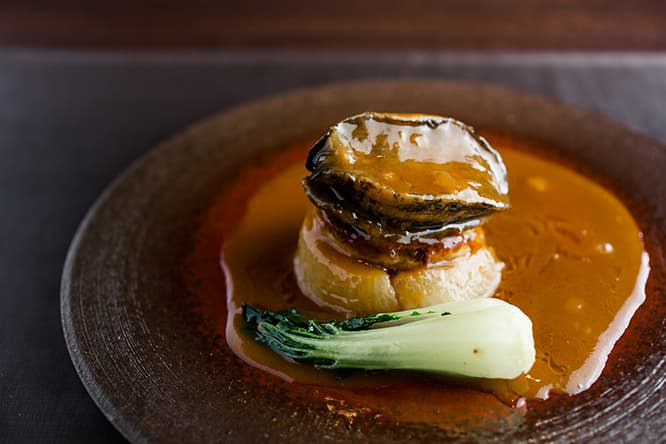 「フレッシュ黒鮑の姿煮込み フォアグラ大根とともに」7,000円。鴨白湯、上湯、オイスターソースなどを合わせたソースがとろり。鮑の磯の香りとフォアグラの甘みとコク、旨みを吸った大根が渾然一体となったスペシャリテだ。