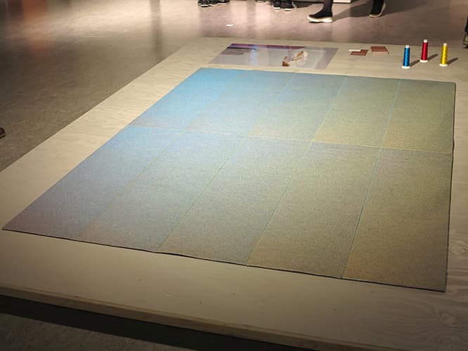 タマラ・ファン・ロイの《Flux Rug》は、三原色の糸で特殊な刺繍を施すことで、視点や光の角度により鮮やかに色が変わる不思議なラグ。