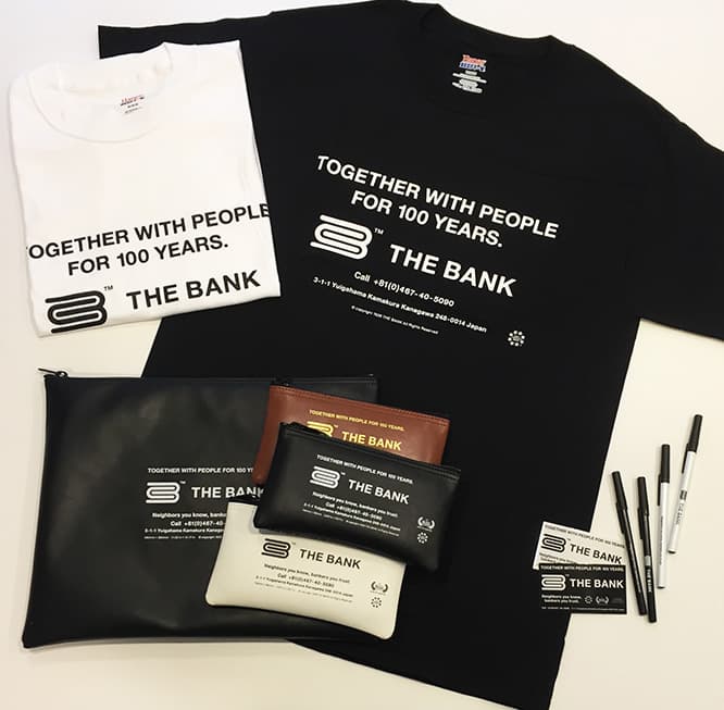《T-SHIRT (黒 / 白)》 XS / S / M / L  4,800円。《BANK BAG LARGE (黒)》 2,800円。《BANK BAG SMALL (黒 / 茶 / 白) 》1,600円。《BIC BALL-POINT PEN (黒 / 白)》200円。《STICKER (黒 / 白) 》200円。
