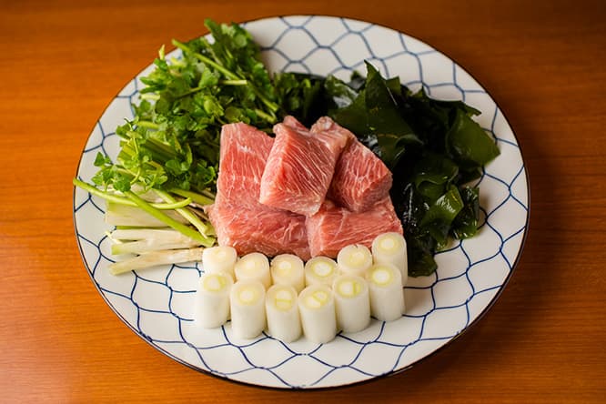 料理は「ねぎま鍋と燻製付のコース」4,300円より（写真は2人前）。ねぎま鍋の具はバチマグロの大トロ、長ネギ、ワカメ、セリ。夏はセリが水菜や壬生菜などに変わる。