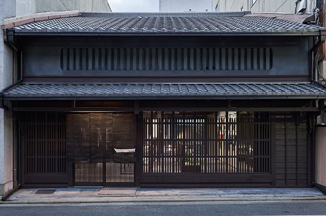 柳馬場通沿いに位置する町家を改修。墨色を基調としたシックな佇まいの向こうに、色鮮やかな服が見える。