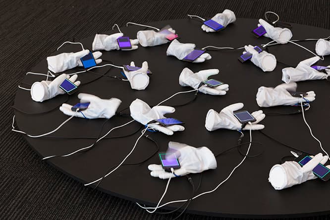 手の平のiPod Touchをある一定の規則に合わせて親指がタッチするインスタレーション《node hands》。綿貫岳海（情報科学芸術大学院大学）によるもの。