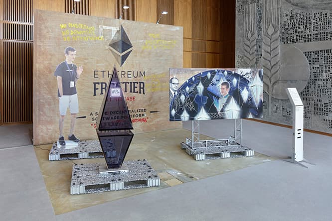 サイモン・デニー《ブロックチェーンの未来予測／フェア用ブースと特別郵便切手：イーサリアム（リンダ・カンチェヴとの共作）》2016 展示風景：第9回ベルリン・ビエンナーレ、ドイツ、2016　撮影：Hans-Georg Gaul　Commissioned and coproduced by Berlin Biennale for Contemporary Art　Courtesy of the artist and Galerie Buchholz Cologne / Berlin / New York（参考図版）