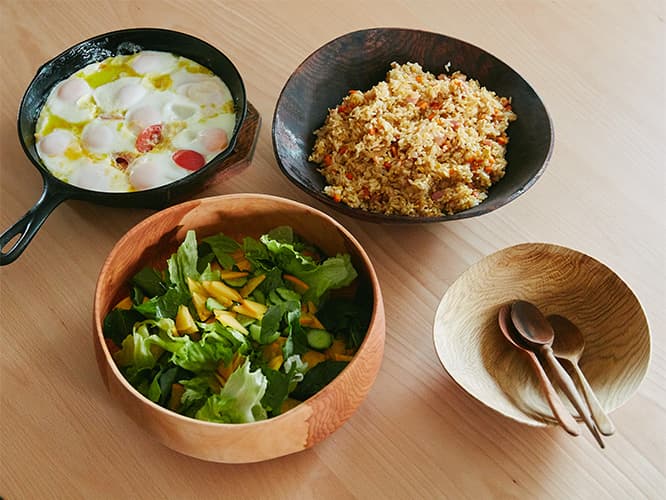 東京・八王子に住居兼工房を構える木工家、須田二郎が作った「ごはんと器」。本日のごはんは3種類のメニューを右下のウッドボウルに盛り合わせていただくランチプレート。左下／〈ウッドボウル・サクラ材〉×緑の野菜と柿のサラダ。左上／卵とトマトのウエボスフラメンカ。右上／〈漆ボウル・ナラ材〉×定番炒飯。レシピは後半でご紹介。