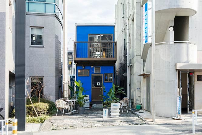 写真中央が、正面壁のみブルーに塗られた〈SKWAT〉の外観。建物が通りから奥まっているので見過ごしがちだが、手前の屋外スペースに積み上げられたコンクリートブロックにロゴがあるので、これを目印にするとわかりやすい。