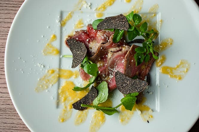 モモ肉をサッとグリルした、いわゆる牛肉のたたき「あか牛のカルパッチョ 黒トリュフとルッコラ」2,400円。トリュフが香るニンニクのアイオリソース、パルミジャーノレッジャーノ添え。