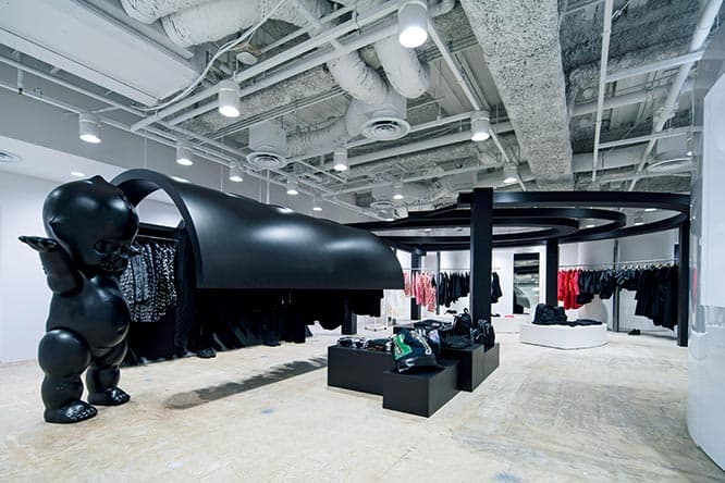 白い空間に黒い什器が異彩を放つ〈BLACK COMME DES GARÇONS〉のコーナー。右手のアーチ下には〈COMME DES GARÇONS〉のアイテムが。