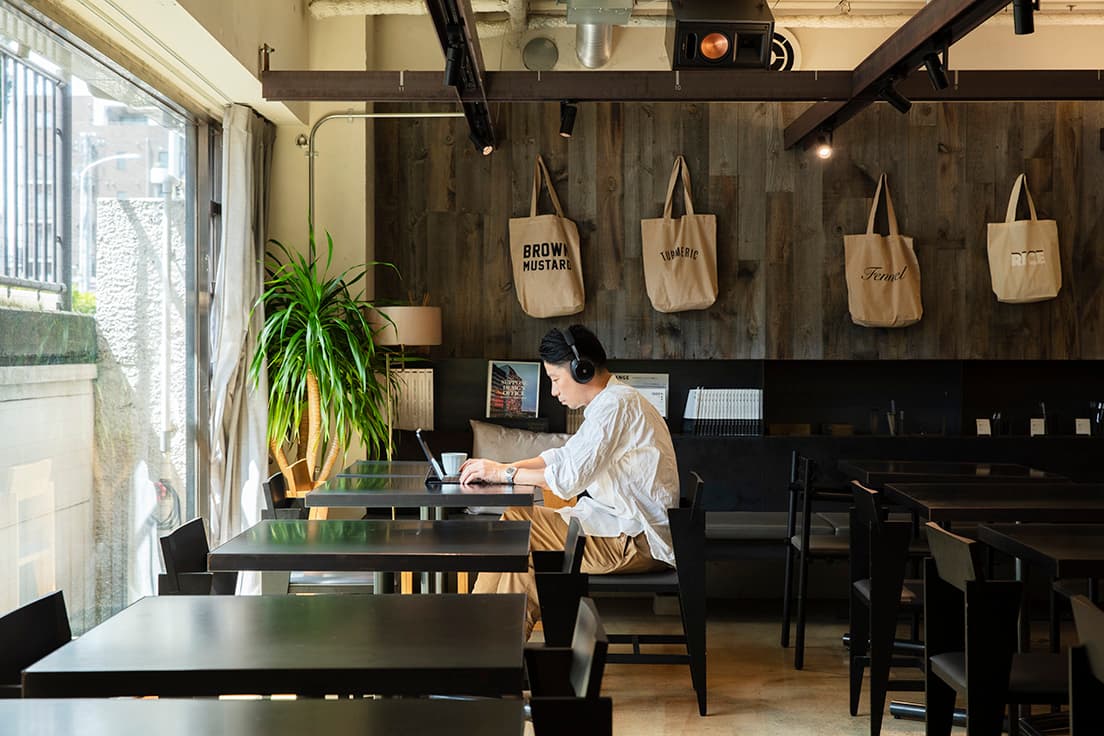 建築設計事務所〈SUPPOSE DESIGN OFFICE〉のオフィスと食堂が一体となった東京・代々木上原の〈社食堂〉で、淹れ立てのコーヒーを飲みながらPCに向かう谷尻さん。仕事中はノイズキャンセリング機能がついたヘッドホンで音楽を楽しむことが多い。アームがスリムでPC作業時も邪魔にならないダイニングチェアは谷尻さんのデザイン。