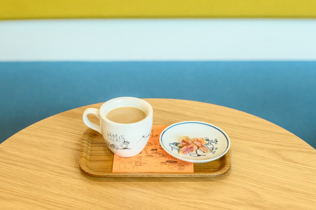 喫茶部でひと休み。全て異なる『サザエさん』のイラストが焼き付けられた喫茶部オリジナルのコーヒーカップ（非売品）の中身は、銀座の老舗コーヒー店の豆を使った「ミルク珈琲（ホット）」400円。お茶うけは、町子が毎日パパイアを好んで食べていたことから生まれた「ドライパパイア」100円。