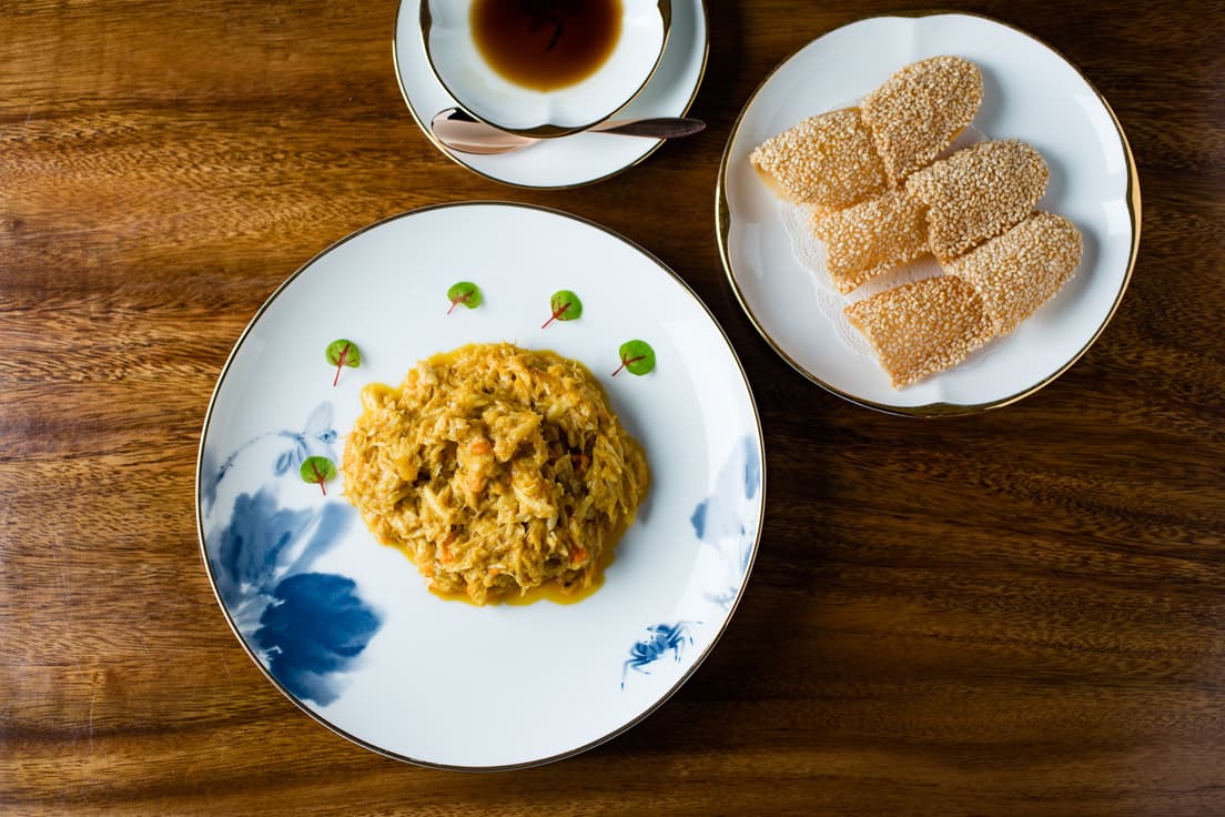 雄蟹の胸肉炒め ポーピン添え10,000円（2〜3人前）。ゴマをまぶした香ばしいポーピン（薄餅）に蟹の身をぎゅっと詰めて食べる。アラカルト、または25,000円／35,000円、50,000円コースに一部登場する。