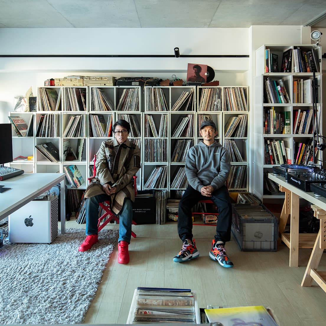 時折開催されるオンラインDJイベントでおなじみ、真鍋大度の仕事部屋を岡村靖幸が訪問。3,000枚のレコードを背に話は尽きない。岡村：コート／180,000円、 Tシャツ31,000円（共にサカイ。TEL03 6418 5977）他はスタイリスト私物。