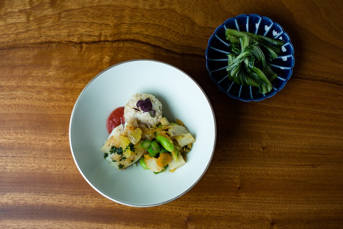 「おわりのお重／本日のお魚のソテー 玄米おにぎり 季節野菜のソテー」。この日の魚はタラ。八角を効かせたルバーブとリンゴ、イチゴのソース添えたり、おにぎりの具がピーカンナッツ味噌だったり、斬新なアイデアが詰まったひと皿。奥の小皿は「広島菜」。