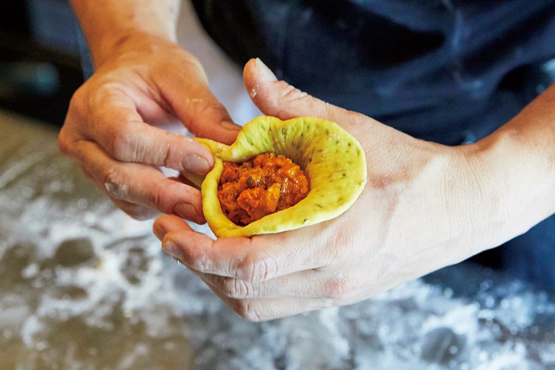 ターメリックで生地も鮮やかな黄色に。冷やし固めたバターチキンカレーを包んでいく。