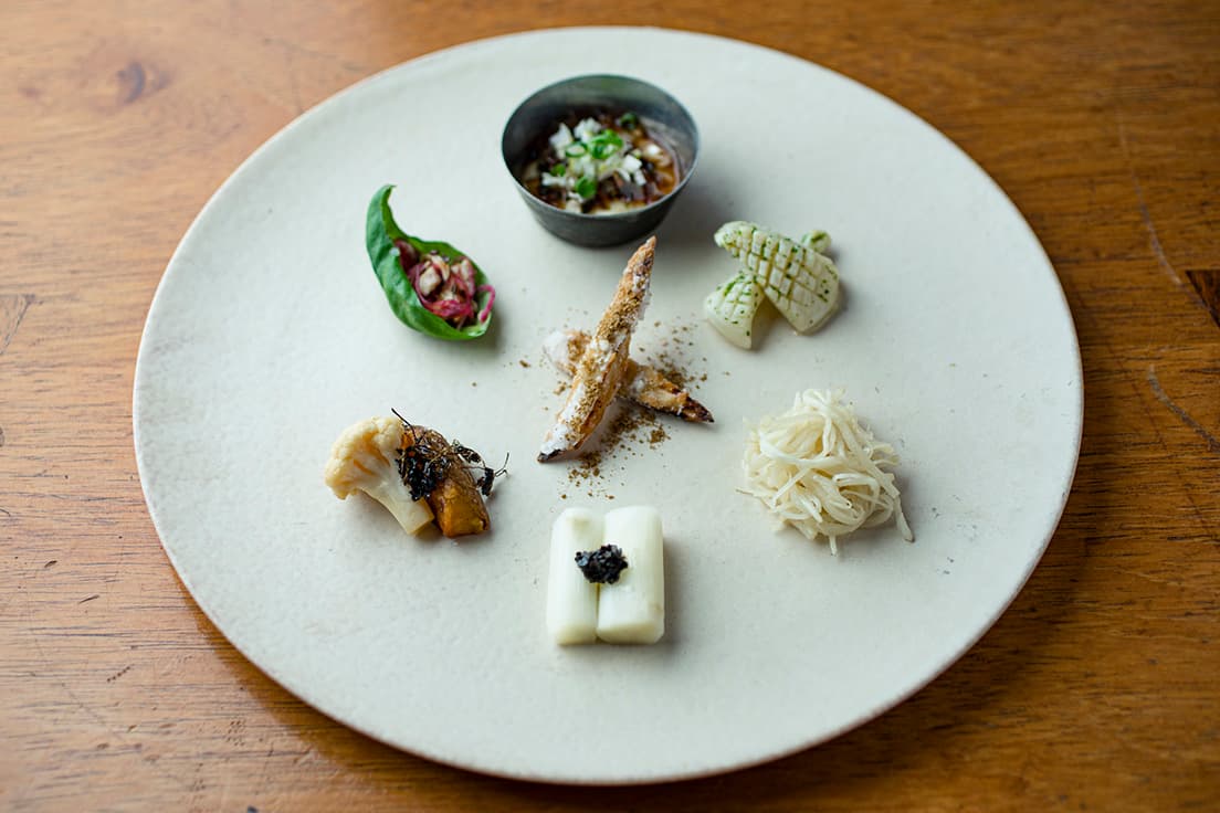 「前菜-8種盛り-」。上から時計回りに「ピータン豆腐-唐辛子-」「アオリイカの冷製 椒麻ソース-花山椒-」「マコモダケとレモングラスのマリネ-レモングラス-」「ホワイトアスパラの生胡椒ソース-黒胡椒-」「カリフラワーのカルダモンピクルス-カルダモン-」「紅芯大根と鶏肉のガパオ和え-バジル-」中央は「ゴボウとクミンの唐揚げ-クミン-」。
