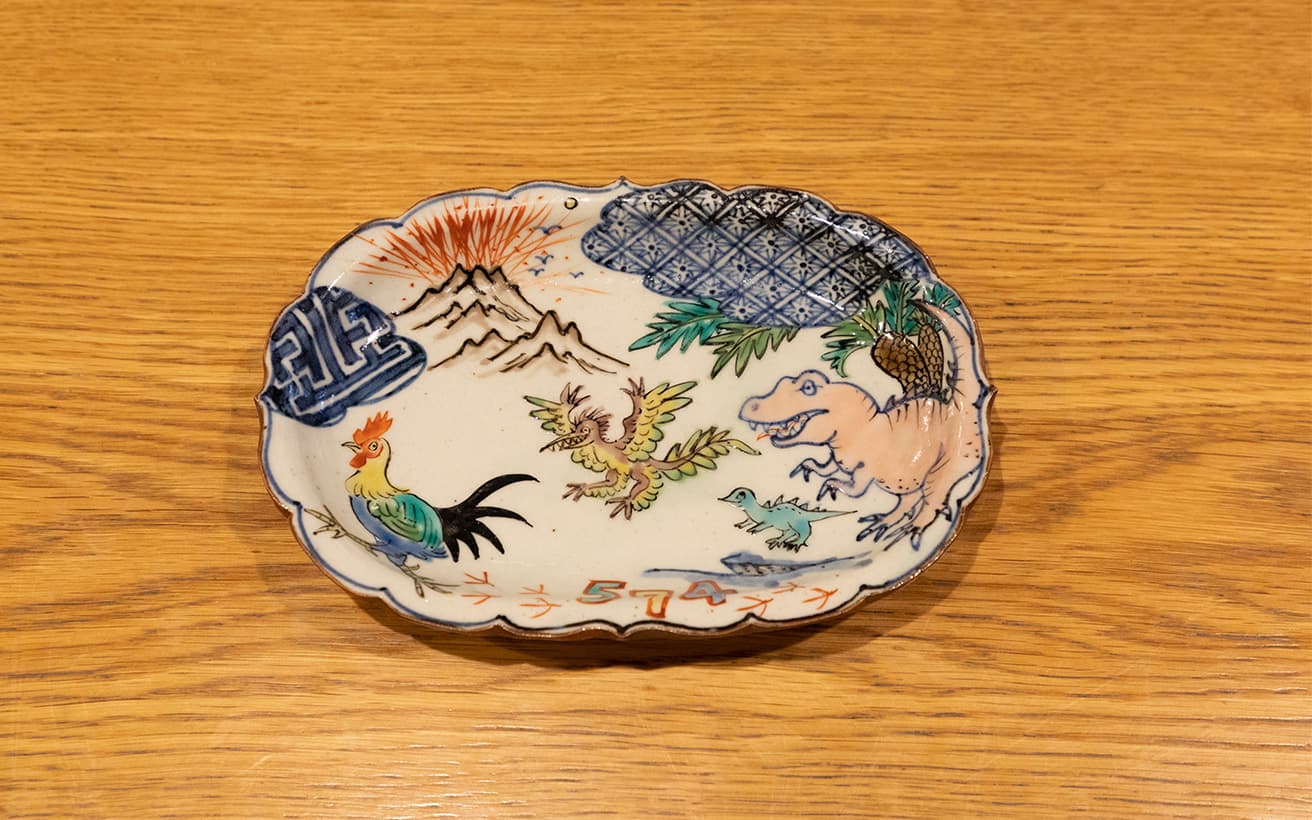 古典的なモチーフとともに、恐竜とニワトリの姿が描かれる。楕円輪花皿20,570円。