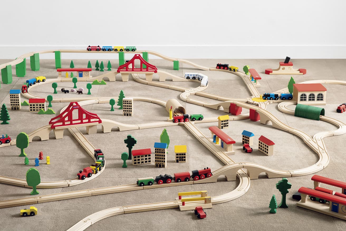 Wooden Train Series（1952）。レールセット1,980円〜4,510円、吊り橋7,920円、鉄橋3,520円、貨車4両4,620円、特急4両4,290円、駅と乗客4,180円、踏切とトラック3,740円、ニュータウン2,640円、エンジンハウス7,040円、トンネル緑3,190円、フェリーボート6,600円 他（以上ミッキィ／アトリエ ニキティキ TEL 0422 21 4015）。床に敷いたタイルカーペット《ウールタイル モカ/プレーン》［1枚50×50cm］各4,950円（堀田カーペット TEL 0725 43 6464）。