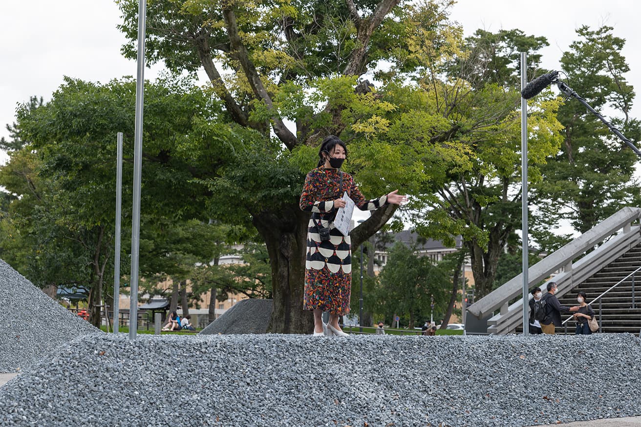 ステージ状に設えた石組の上で解説する岩瀬諒子。テントが架けられるように3本のポールが伸びている。