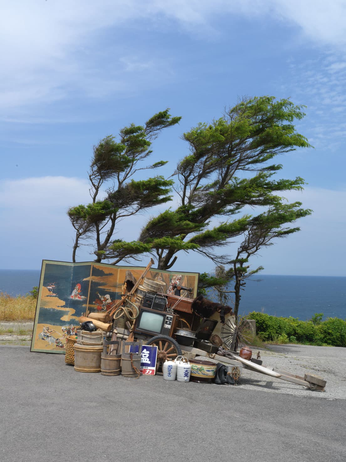 石川直樹《奥能登半島／珠洲全景》。海辺に珠洲市の家や蔵から出てきた家具や家電が並べられている。人々の少し前の暮らしを思わせる。　photo_Naoki Ishikawa