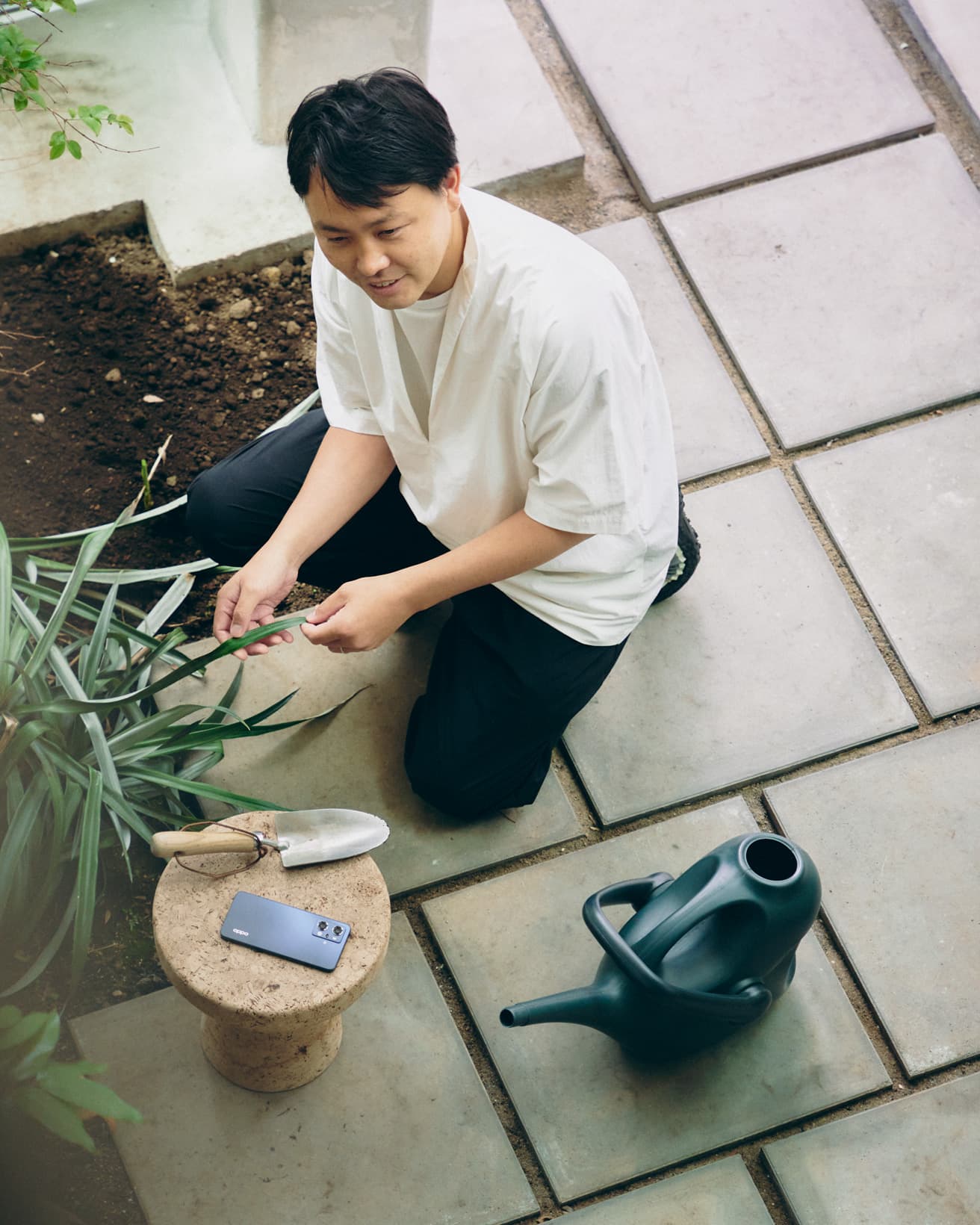 建物内に地植えしたパイナップルを手入れする齊藤。かたわらには《OPPO Reno7 A》が。
