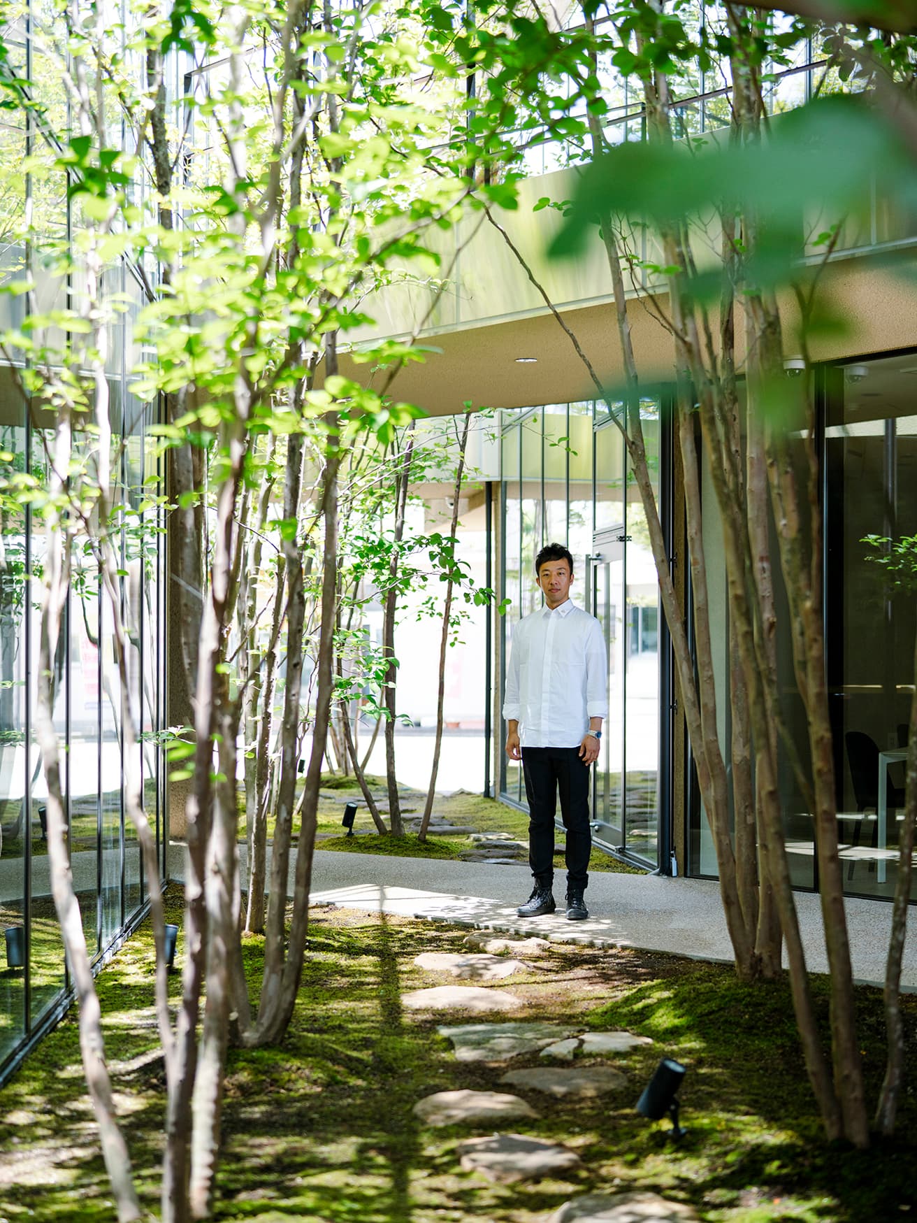 2つの道の交差地点に立つ奈良。建物が緑道で4つに分かれる、複雑な構成が豊かな空間体験を生み出す。樹木は上部に枝を広げる夏椿。敷石は金沢城の石垣にも使われる戸室石（とむろいし）。「金沢という街の文化を踏襲し、内に開く建築です」