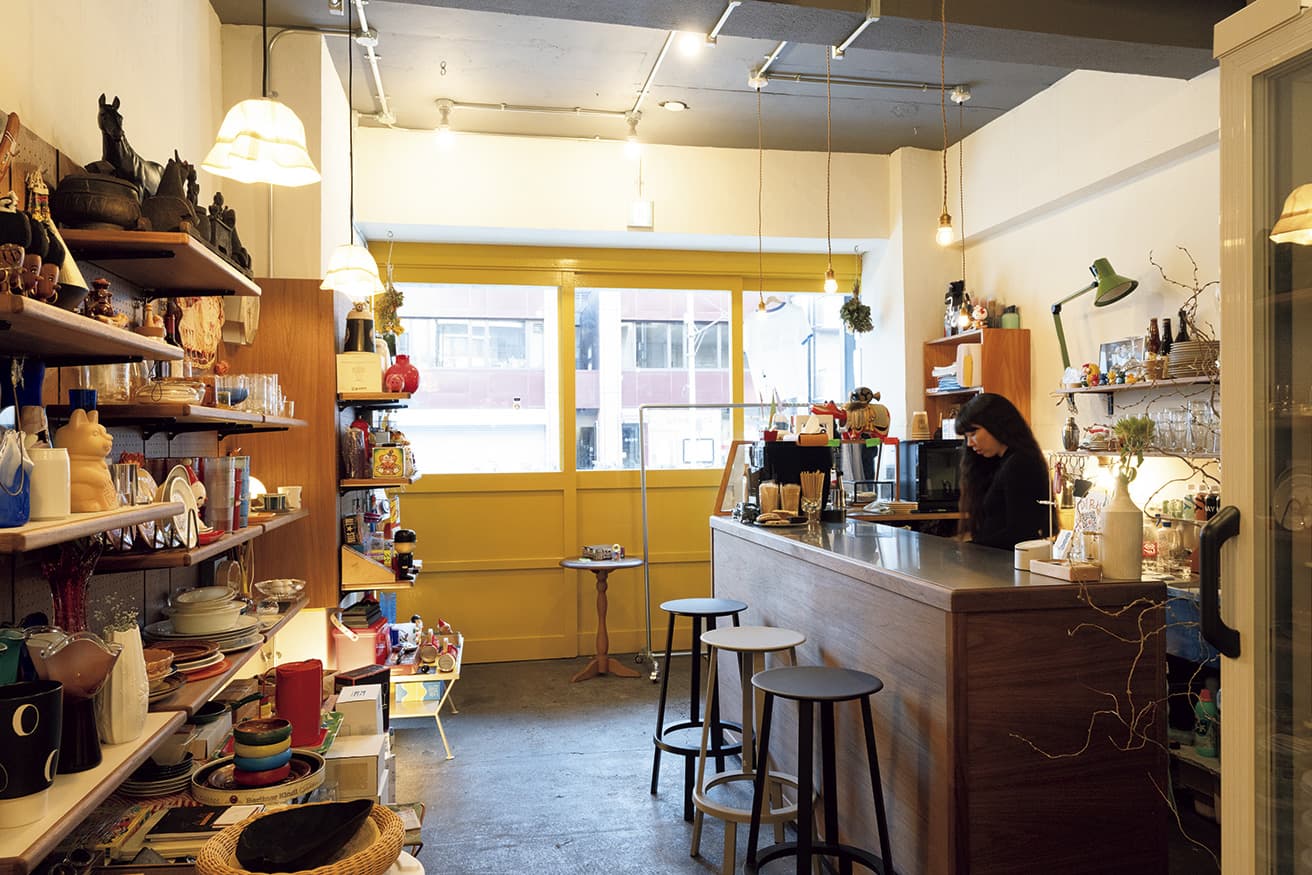 手前側には雑貨類が並ぶ。カフェ＆バースタンドでは、昼には焼き菓子、夜はつまみ類も楽しむことができる。