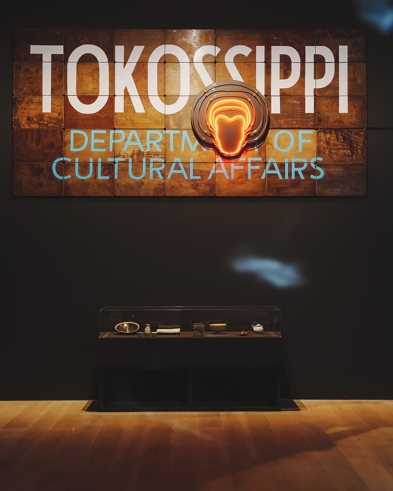 シアスター・ゲイツの木製看板の作品《TOKOSIPPI文化事業局》（2024年）とネオン作品《アフロ・ネオン》（2018／2024年）を組み合わせて展示。“TOKOSIPPI”はゲイツがルーツを持つミシシッピ州と常滑をかけあわせた造語。その下にはルーシー・リーなどゲイツの集めたコレクションが。