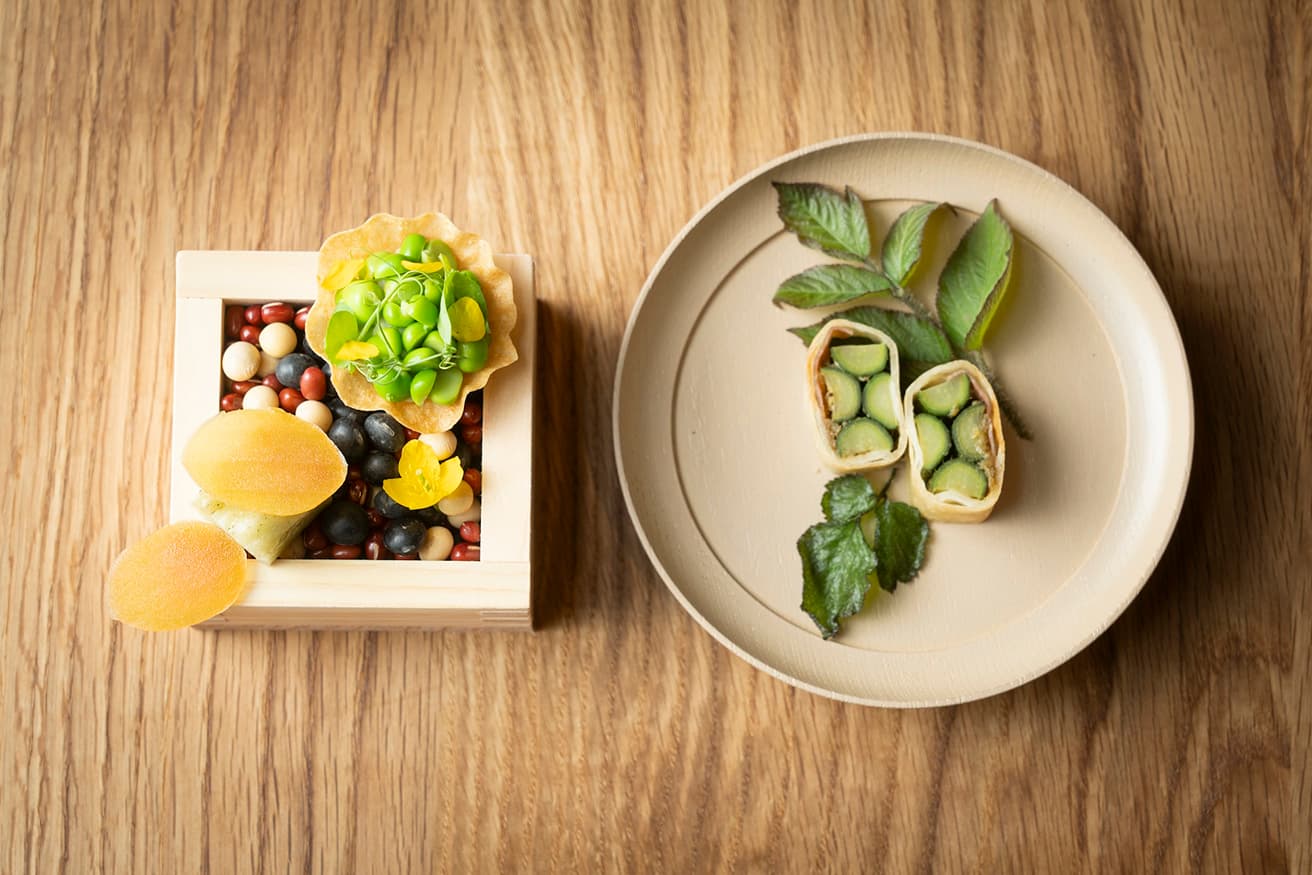 アミューズ「小さな豆のタルト カラスミ餅 独活（ウド）春巻き」。春の珍味からコースはスタート。春の訪れをあらわす若い豆、地元の日本酒蔵〈笹一酒造〉の最高級銘柄《旦》に漬け込んだカラスミ、ウドと蕗味噌を5年熟成の生ハムで巻いた春巻き。