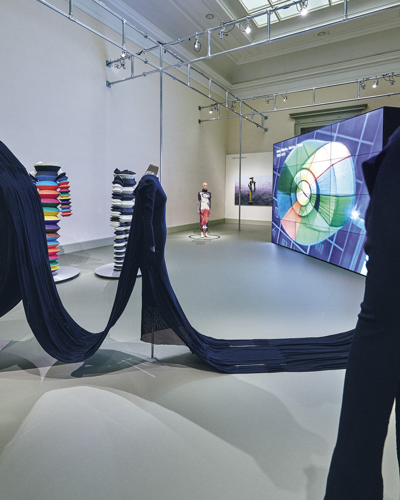 衣服とデザインの領域を自由に横断した革命児（左ウィング）。1998年の『ISSEY MIYAKE Making Things』展では〈PLEATS PLEASE〉のドレスを天井からぶら下げてモーターで上下動させるなど、ユニークな展示が話題に。本展会場ではロール状のテキスタイルから製造されるドレスを展示。奥には森村泰昌との作品が。