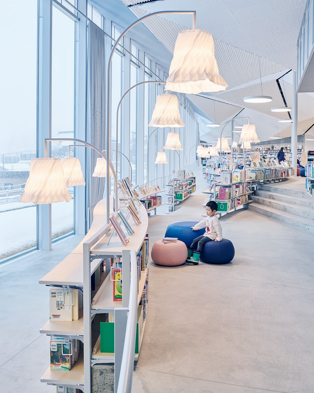 書架がカーブを描く「こどもとしょかん」。床は周囲より低く、敷地を引き継いだ勾配がある。照明はオリジナルで、天井同様に和紙を用い、小千谷縮を意識したデザインだ。