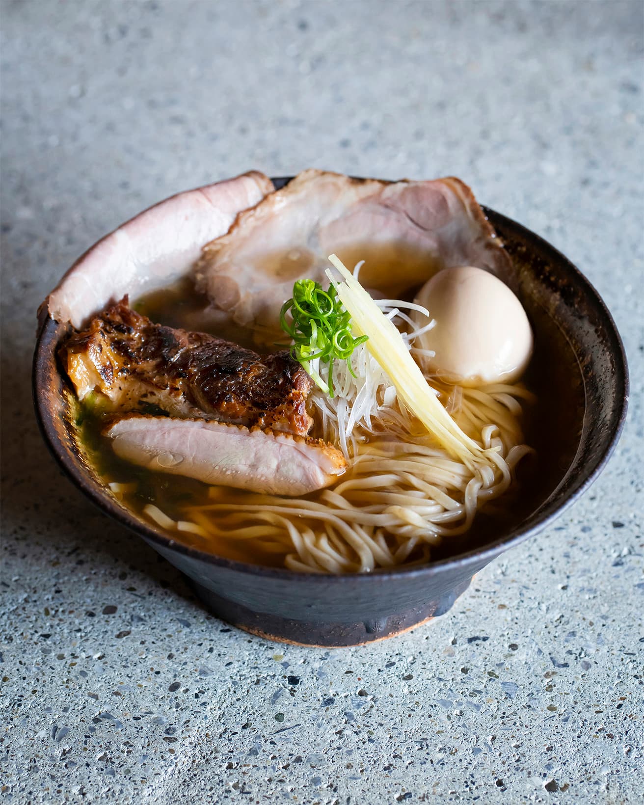 店の看板メニューのひとつ〈特上 EIBUNそば【黒】〉1,480円。大正屋醤油を使ったかえしを出汁に加えたスープでこだわりの麺を。トッピングは〈EIBUN〉といえばお馴染みの炙り軟骨と、塩豚肩ロース＆鴨ロース。中央には刻みネギ、ハリ生姜、磯の香りを添えるアーサーも潜む。濃厚なコクと風味の味玉は、栄文さんが「ようやく出合った」と言う八重瀬町「新寿卵」を使用。