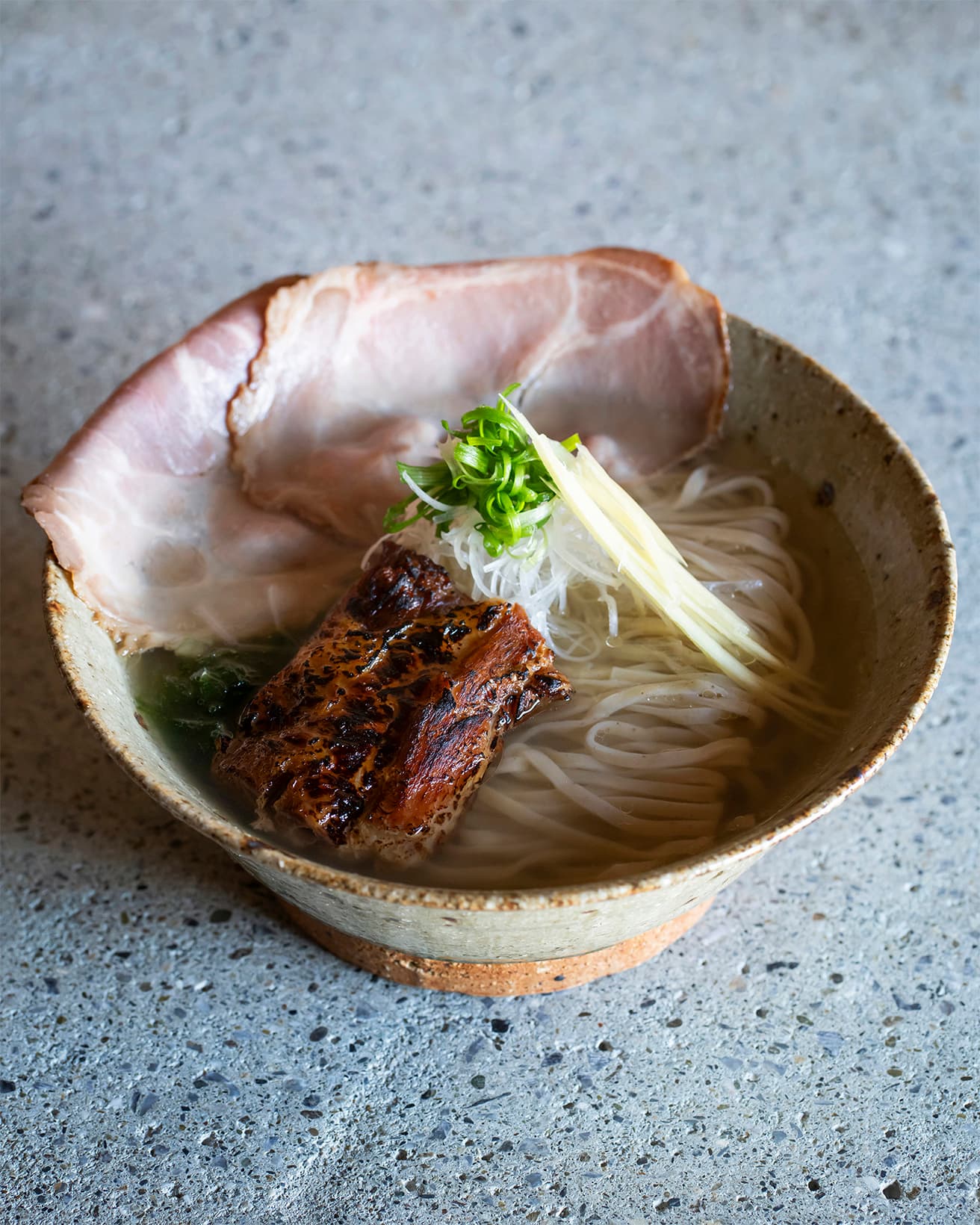 同じ仕立てを出汁本来の風味＋鶏油のスープで味わう〈特上 EIBUNそば【白】〉1,480円。味変には〈EIBUN〉自家製コショウがおすすめ。店オリジナルの器はすべて南城市で作陶する宮城正幸さんによるやちむん（焼きもの）だ。