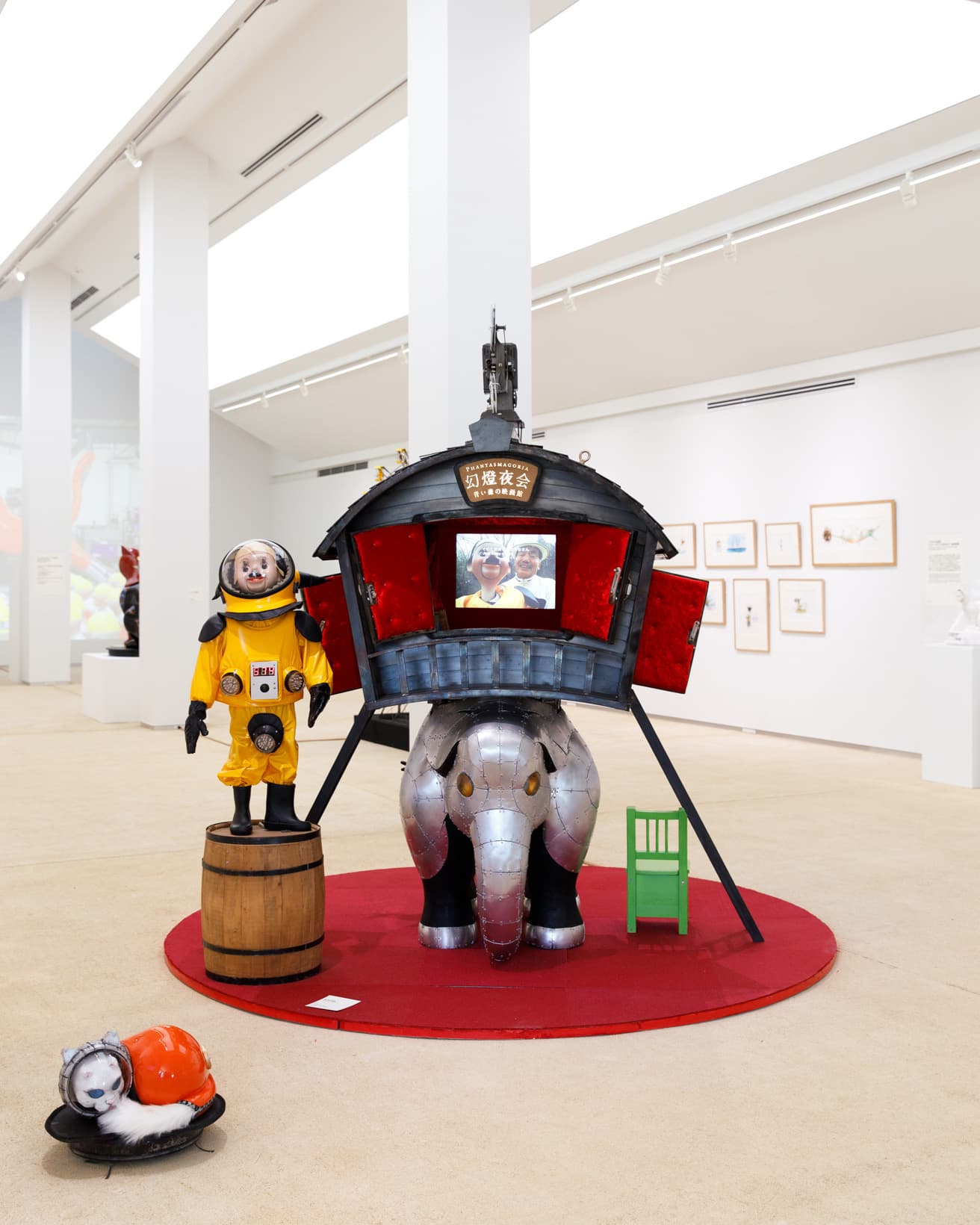 2003年、万博記念公園内の国立国際美術館（現在は中之島に移転）での展覧会『メガロマニア』にて誕生したキャラクター「トらやん」。ヤノベさまのお父さまが、チェルノブイリ探訪の際に制作された作品《アトムスーツ》の幼児版《ミニ・アトムスーツ》を着た腹話術人形「トらやん」を演じます。コチラは堅牢なシェルターで覆われた象とその背中に乗った子供用映画館から構成されます立体作品《青い森の映画館》（2006）。映画館では核攻撃から生き延びるためのサバイバルを孫たちへ伝授する教育番組が上映されてございます。