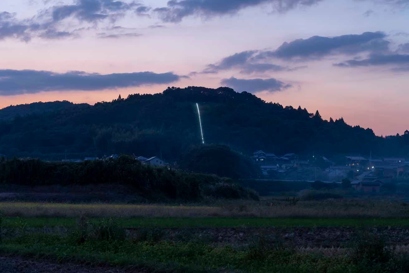 島袋道浩が制作した、山の頂まで続く階段のない参道《光る道》。一直線の手すりが設置されており、夕刻になるとライトアップされる。photo_Takashi Kubo 
