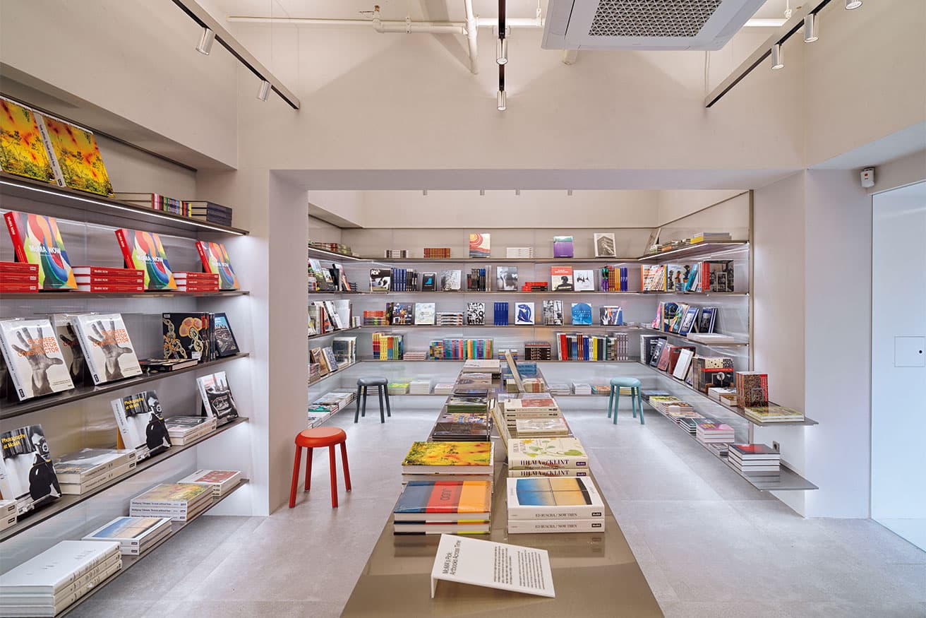 淡いグレーの思索的な書籍ホールから光沢ある暖色が基調のデザインストアへ雰囲気を変える色使いが卓越。