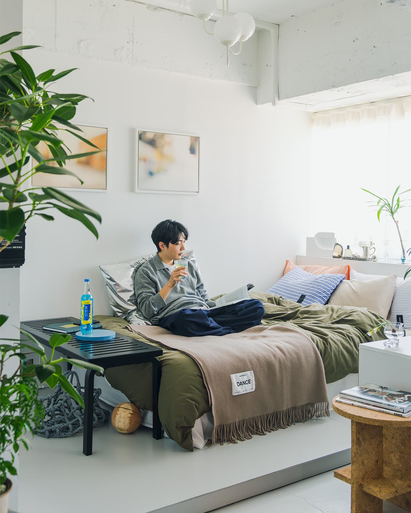 ベッドをソファがわりにしてジャスミン茶割りを片手に読書を楽しむ竹内さん。背もたれには〈マグニバーグ〉のビッグクッションを。