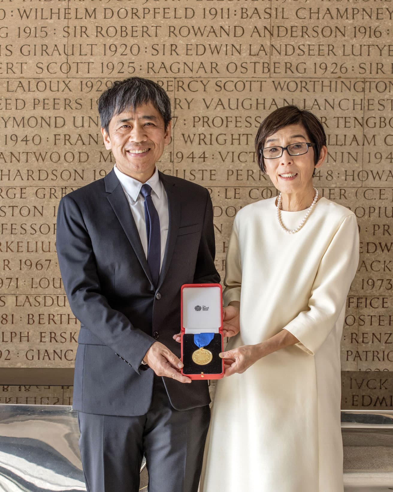王立英国建築家協会のエントランスの歴代のゴールドメダル受賞者の名が刻まれた壁を背景に、SANAAの妹島和世と西沢立衛。© Morley von Sternberg 
