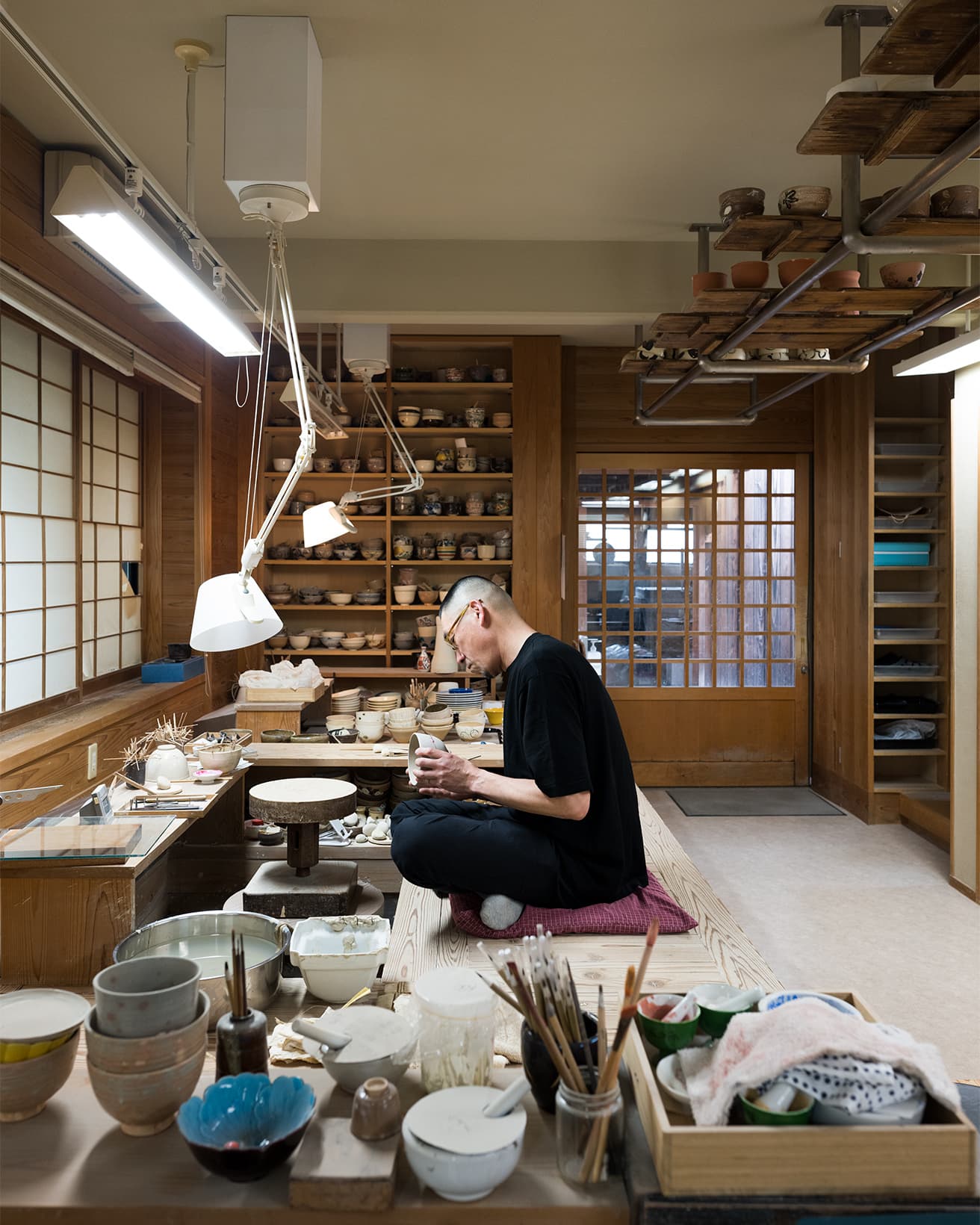 永樂さんの仕事場にて。 1階は轆轤（ろくろ）、下絵の仕事を中心に作業している。背後の棚に何げなく並べられているのは、歴代の作品。
