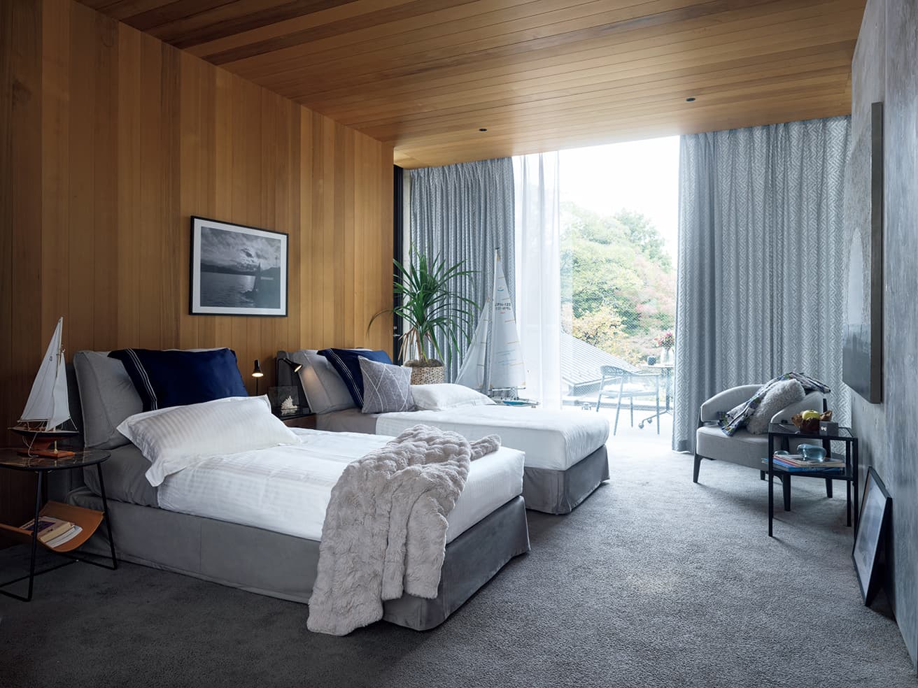 ニトリが用意する《ホテルスタイル》の寝具には、枕、掛け布団、カバーリング（枕、掛け布団、マットレス）と上質の眠りを約束してくれるアイテムが揃っているだけでなく、ベッドスカートもオーダーできるのが嬉しい。まるでホテルのようなベッドルームが自宅に誕生し、リラックスできる時間を過ごせるはずだ。ベッドフレームシングル（Ｗ99×Ｄ215×Ｈ91㎝）39,990円、ベッドスカート（Ｗ99×Ｄ215×Ｈ26㎝）14,000円、掛ふとんカバーセミダブル4,490円、ベッド用クッションシングル5,990円、まくらカバー1,190円、クッションカバー（奥側ベッド上）999円、サイドテーブル（ベッドの間）19,990円、デスクライト3,990円、アクセサリーボックス1,990円、ポスターフレームA1（左）2,990円、カフェテーブル（ベランダ）（Ｗ60×Ｄ60×Ｈ70㎝）11,990円、マグ（カフェテーブル上）999円、フラワーベース（カフェテーブル上）1,490円、1人用ソファ（Ｗ76×Ｄ68×Ｈ72㎝）39,990円、クッションカバー（ソファ上）1,490円、サイドテーブル（右）（Ｗ40×Ｄ40×Ｈ55㎝）9,990円、置き時計1,490円（電池別売り）、ポスターフレーム（40×50㎝）（右）1,490円（以上ニトリ）。テーブルに置かれたモデルシップ、書籍、各種アイテム、ポスターフレームの中の写真、プラント、プラントカバー、ジャケットなどはスタイリスト私物。