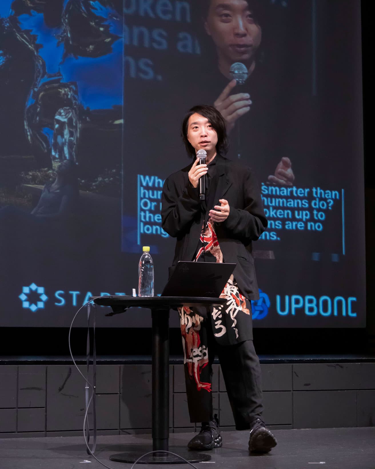 東京・八芳園のステージでの落合陽一。足元はミャク味のあるスニーカー。 photo_Keiko Nakajima 