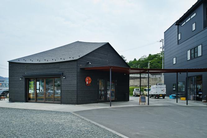〈K-port〉は、同じく伊東豊雄が設計した隣接の磯屋水産と屋根でひと続きになっており、漆黒の外観で統一されている。