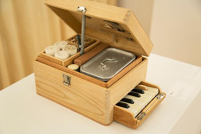 古い木製の救急箱の表面を削った箱の中に、アルミの弁当箱や包帯などを収めて、下部の引き出しにトイピアノを合体させた《救急箱ピアノ 外科用》。2015年制作。