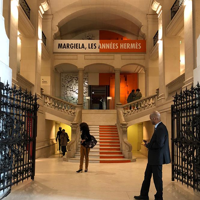 『マルジェラ、エルメス時代』が開催中の〈パリ装飾芸術美術館〉エントランス。こちらはオレンジ＆ホワイトカーペット。会場入り口にもエルメスのオレンジボックスとメゾン マルタン マルジェラのホワイトボックスが積み重なっている。