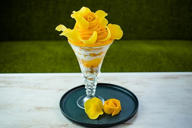 黄色のバラの花びらを添えた「宮崎マンゴーの贅沢パフェ」5,000円（2〜3人前）。ライムでマリネしたマンゴーやココナッツミルクで煮たもち米、ココナッツのアイスなどを重ねたトロピカルな味わい。