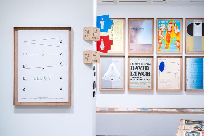 本展覧会のポスター（左）と、これまでにグラフィック・デザインを手掛けたポスターの数々が掲示されているほか、ピクトグラム、サイン、パッケージなども展示されている。