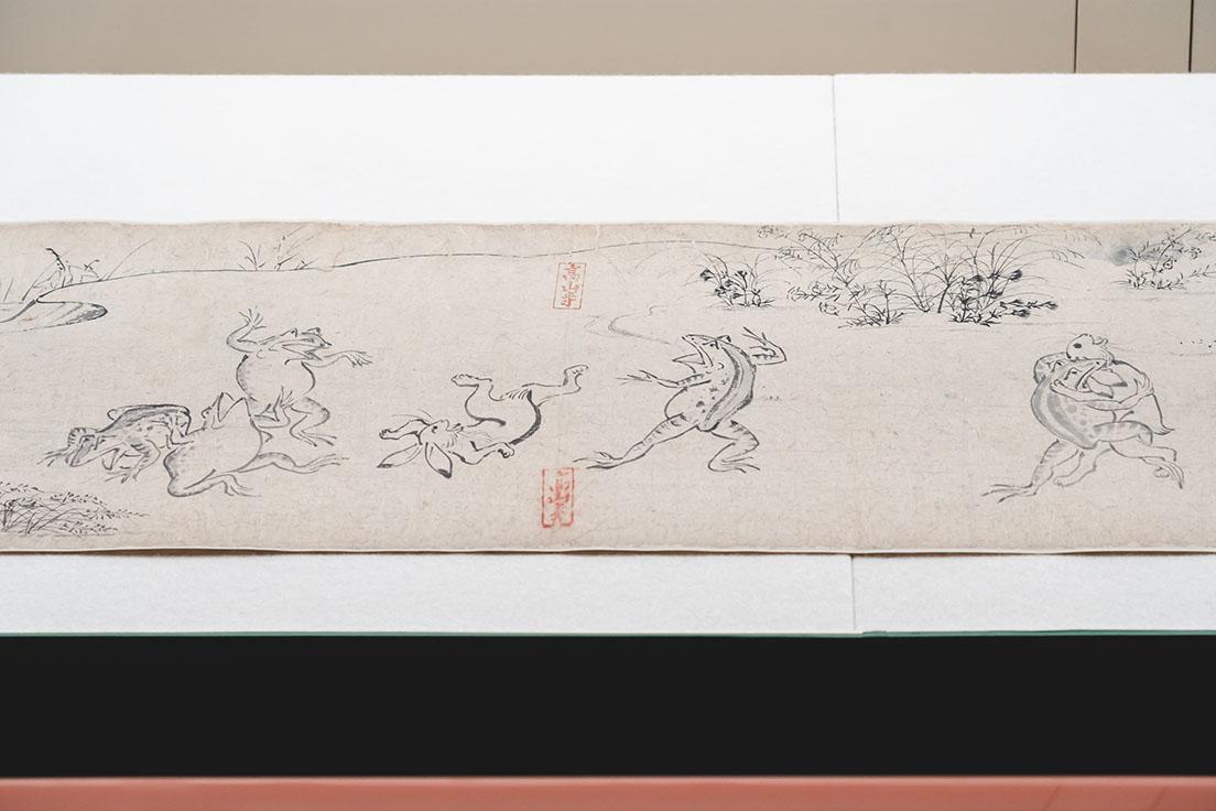 《鳥獣戯画》甲巻（部分、平安時代、12世紀）、ユーモラスなうさぎと蛙の相撲。蛙はうさぎの耳にかみつくという禁じ手を繰り出している。すぐ左には蛙がうさぎを投げ飛ばす場面。時間の流れがひとつの画面で表される。
