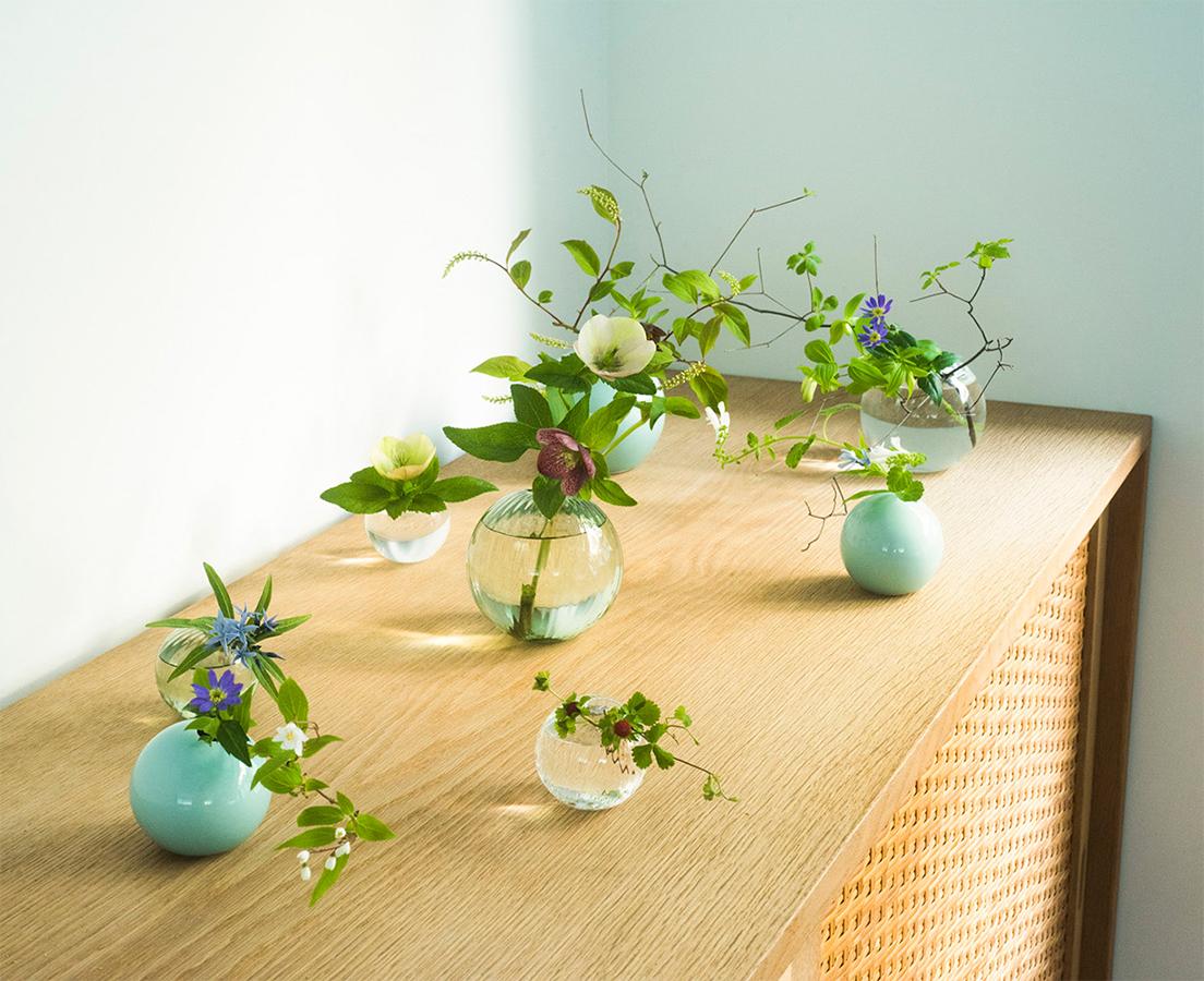ブルーが涼しげな鍋島虎仙窯による青磁の花器は、素地が透ける口縁のグラデーションも美しい。ガラスの花器は菅原工芸硝子が製作し、ストライプのレリーフを施したタイプと無地のタイプがある。青磁各5,000円〜15,000円、ガラス各4,400円〜5,400円（ワン フラワーウェア 公式サイト）　photo_ Yudai Kusano